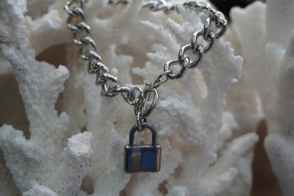 Silver-tone curb-link bracelet with a padlock charm and ring-and-bar clasp.
