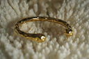 Alternate view: gold-tone open cuff with a rounded profile, rounded ends and dimpled surface.
