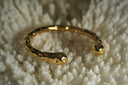 Gold-tone open cuff with a rounded profile, rounded ends and dimpled surface.