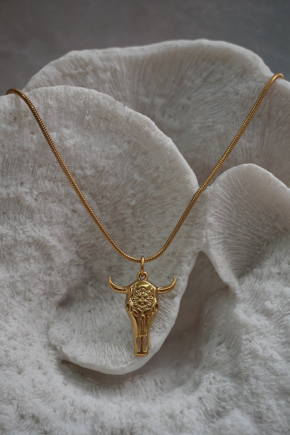Alternate view: gold-tone necklace with an elongated skull pendant, floral forehead pattern and outward-curving horns.