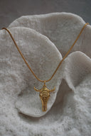 Alternate view: gold-tone necklace with an elongated skull pendant, floral forehead pattern and outward-curving horns.