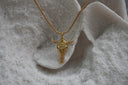 Gold-tone necklace with an elongated skull pendant, floral forehead pattern and outward-curving horns.