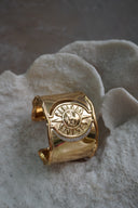 Broad gold-tone open cuff with a raised sun-face motif, rays and curved cut-outs.