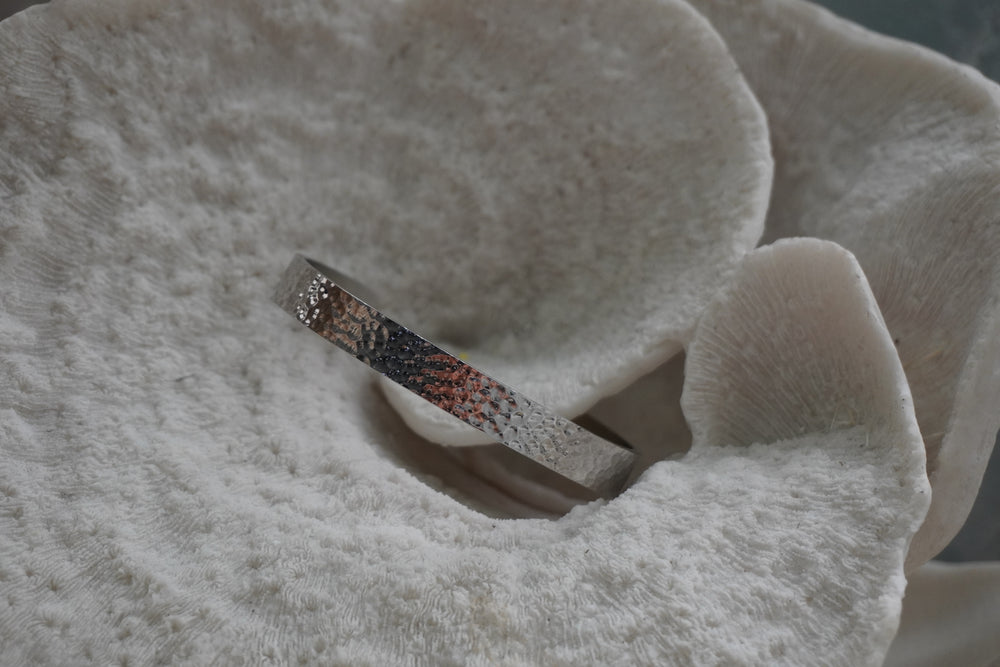 Silver-tone narrow open cuff with a dimpled reflective surface.