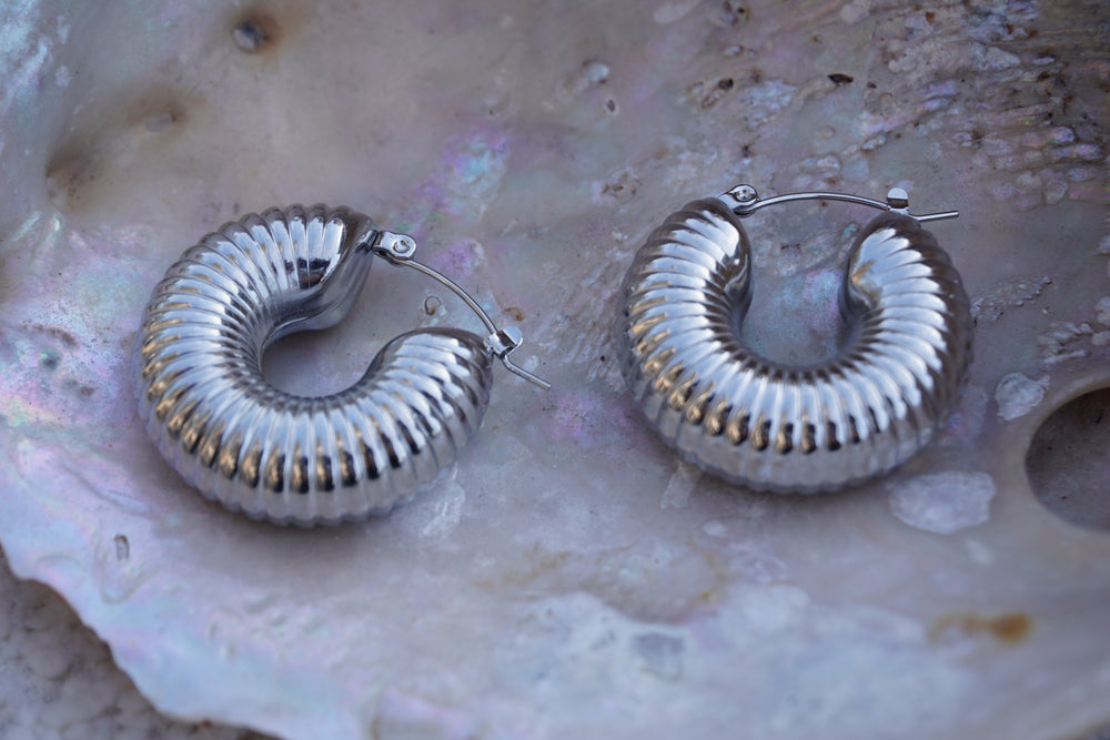 Alternate view: broad silver-tone hoops with fine radiating ribs and rounded contours.