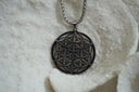 Silver-tone necklace with an open disc pendant featuring intersecting triangles over a circular lattice.