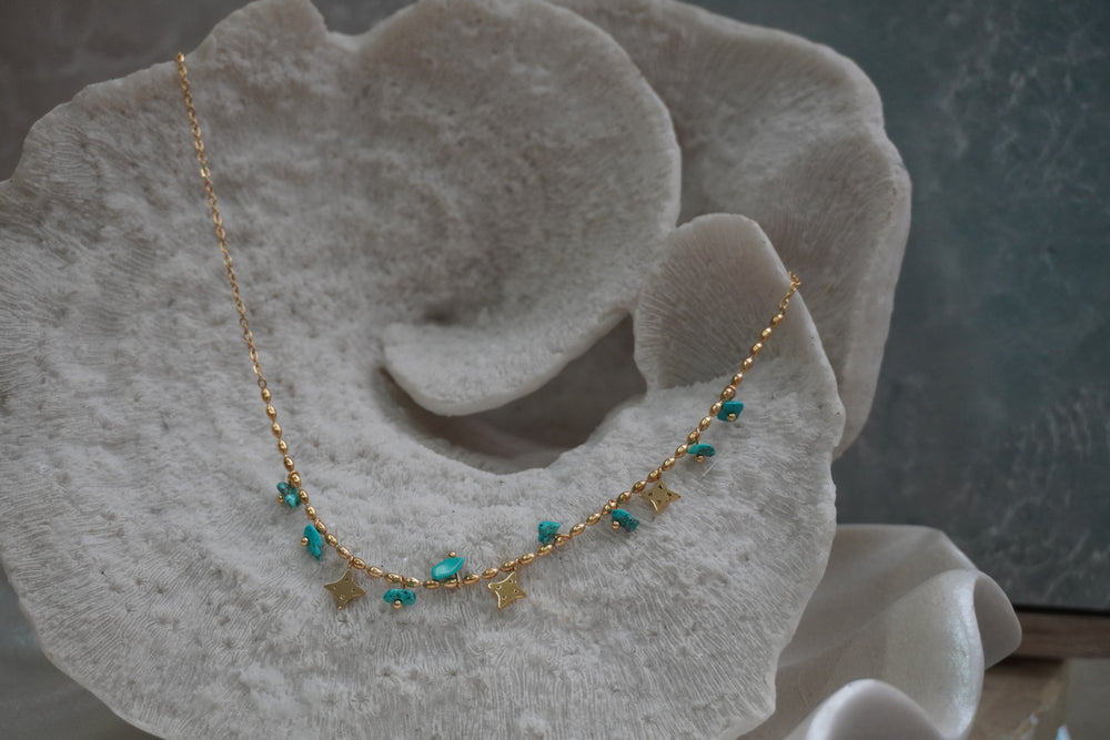 Gold-tone necklace with oval chain details, irregular blue bead drops and four-point star charms.