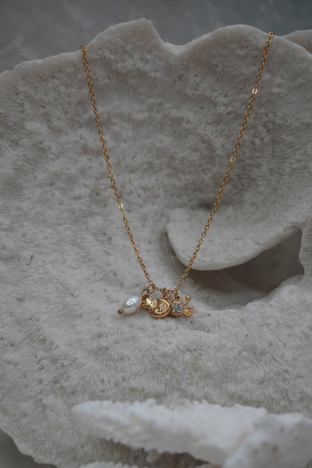 Gold-tone chain necklace with two fish charms, clear accents and a white oval bead.
