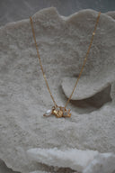Gold-tone chain necklace with two fish charms, clear accents and a white oval bead.