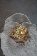 Alternate view: broad gold-tone open cuff with a central sunburst motif, geometric markings and ribbed borders.