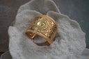 Broad gold-tone open cuff with a central sunburst motif, geometric markings and ribbed borders.