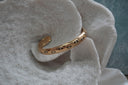 Alternate view: gold-tone open cuff with black eye motifs, white centres and raised radiating details.