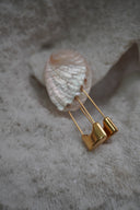 Gold-tone earrings with elongated safety-pin silhouettes and broad curved lower sections.