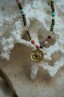 Alternate view: beaded necklace with a gold-tone textured disc, eye motif and green centre.