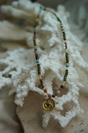 Beaded necklace with a gold-tone textured disc, eye motif and green centre.