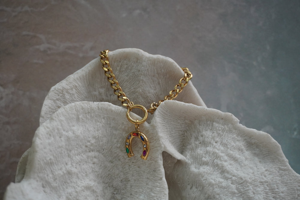 Gold-tone chain bracelet with a horseshoe charm set with multicoloured accents beneath a round connector.