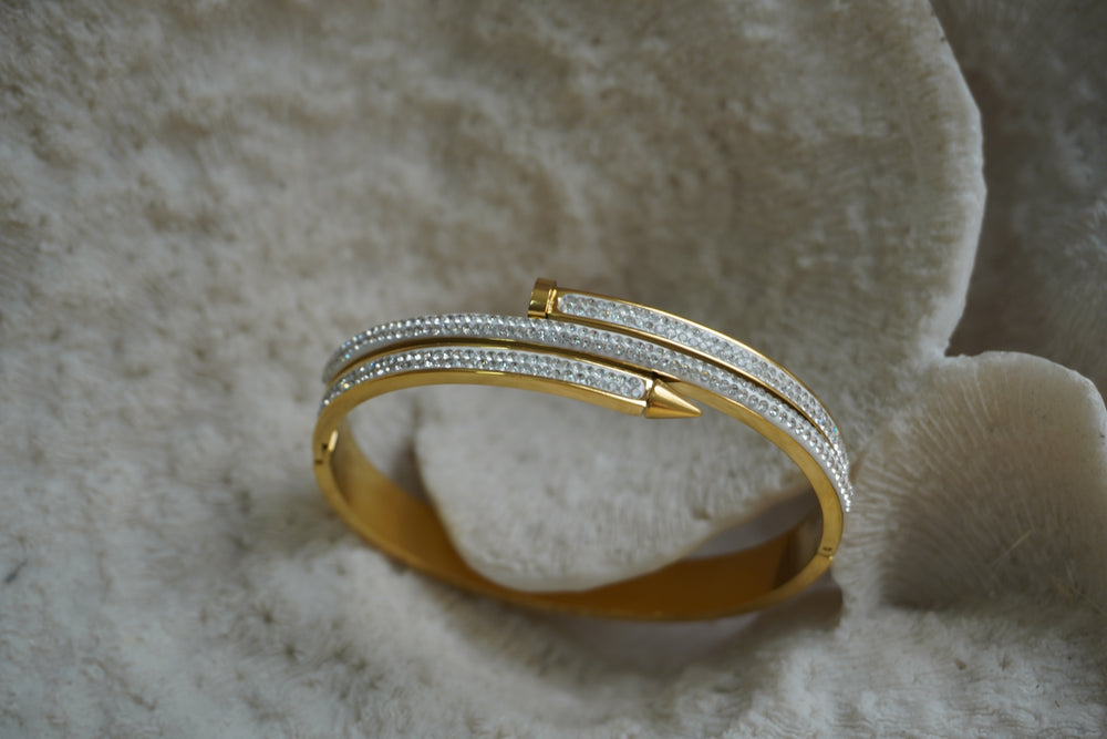 Gold-tone hinged bangle with overlapping nail-like bars and rows of small clear accents.