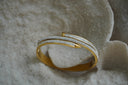 Gold-tone hinged bangle with overlapping nail-like bars and rows of small clear accents.