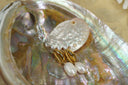 Gold-tone cowrie-motif stud earrings with textured central openings and white oval bead drops.