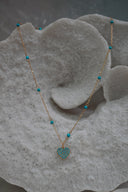 Gold-tone necklace with spaced blue beads and a heart pendant covered in small blue circular accents.