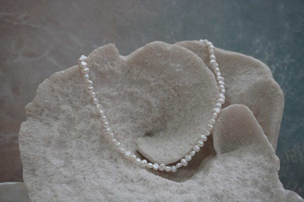 Necklace of closely strung irregular white beads with an iridescent appearance.