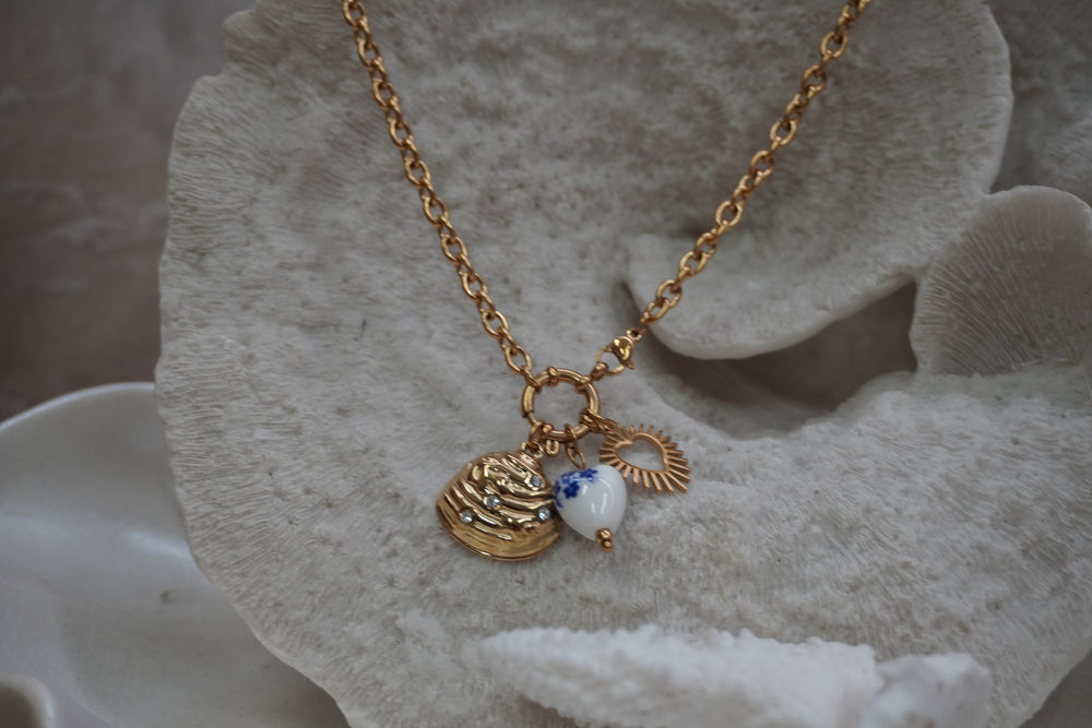 Alternate view: gold-tone necklace with a ridged shell charm, radiating open heart and white heart bead with blue flowers.