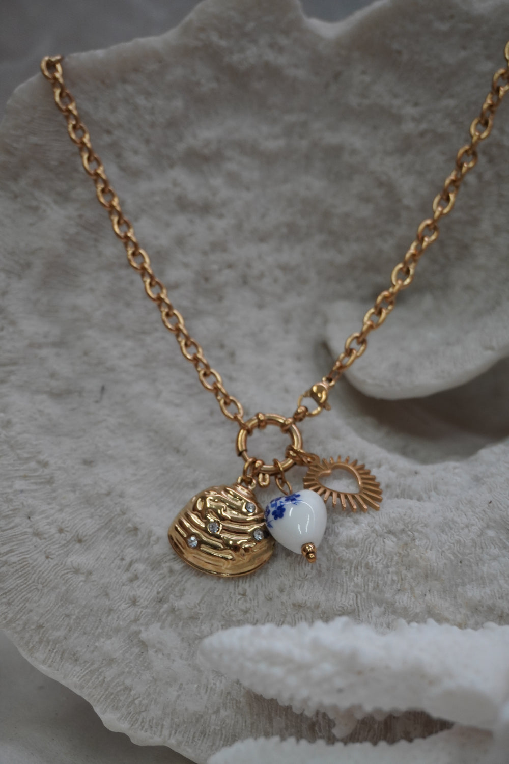 Gold-tone necklace with a ridged shell charm, radiating open heart and white heart bead with blue flowers.