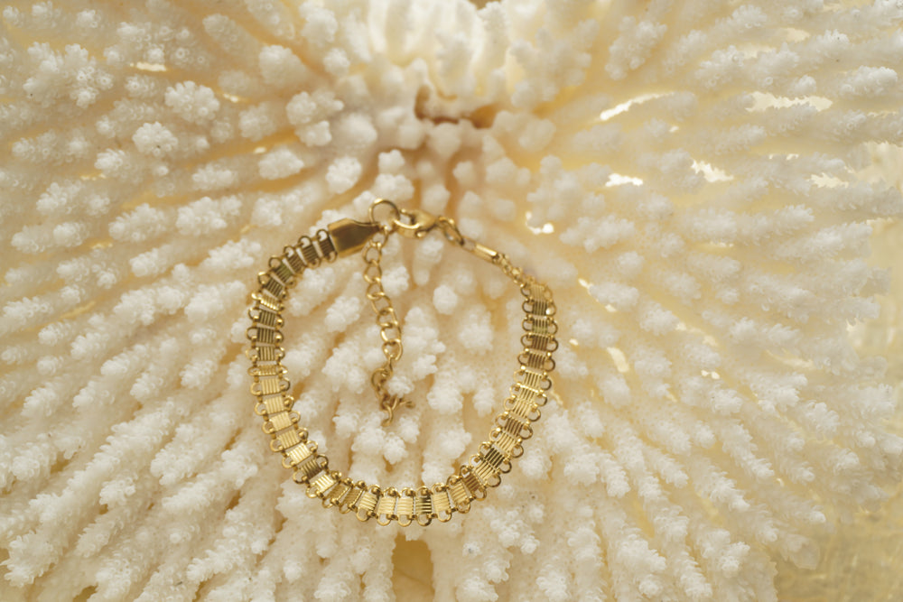 Gold-tone bracelet with ridged rectangular panels, looped edges and an extension chain.