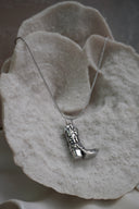 Silver-tone necklace with a western boot pendant featuring raised scroll details and a pointed toe.