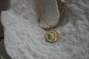 Gold-tone disc necklace with a desert landscape, cactus motifs, green accents and a scalloped pendant edge.