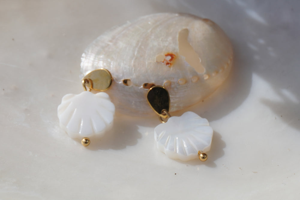 White scallop-shaped drop earrings with gold-tone studs, radiating grooves and rounded accents.