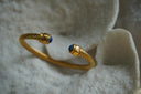 Gold-tone open cuff with rope-like ridges and rounded blue accents at both ends.