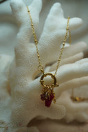 Gold-tone bead-station necklace with a circular centre and a cluster of deep red accents and small charms.