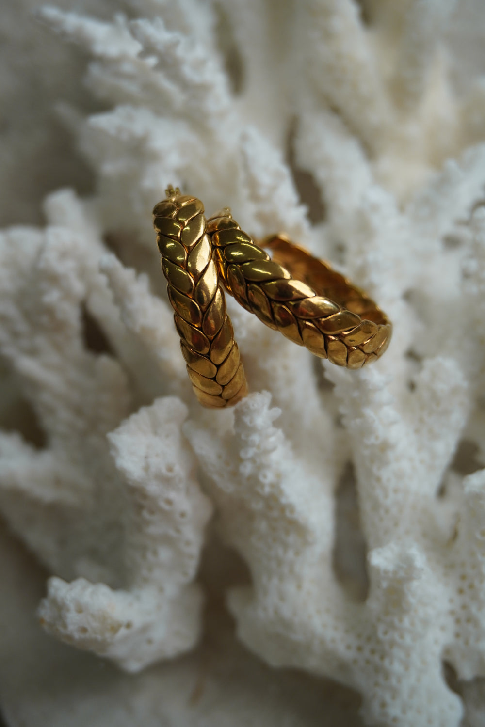 Gold-tone hoop earrings with a raised plaited pattern of overlapping leaf-like shapes.
