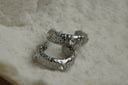 Alternate view: silver-tone broad open hoops with round clear accents, raised borders and dotted texture.