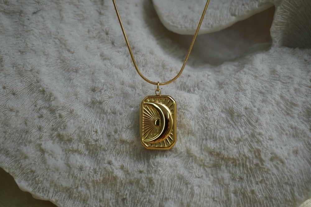 Gold-tone necklace with a rectangular crescent-moon and ray pendant.