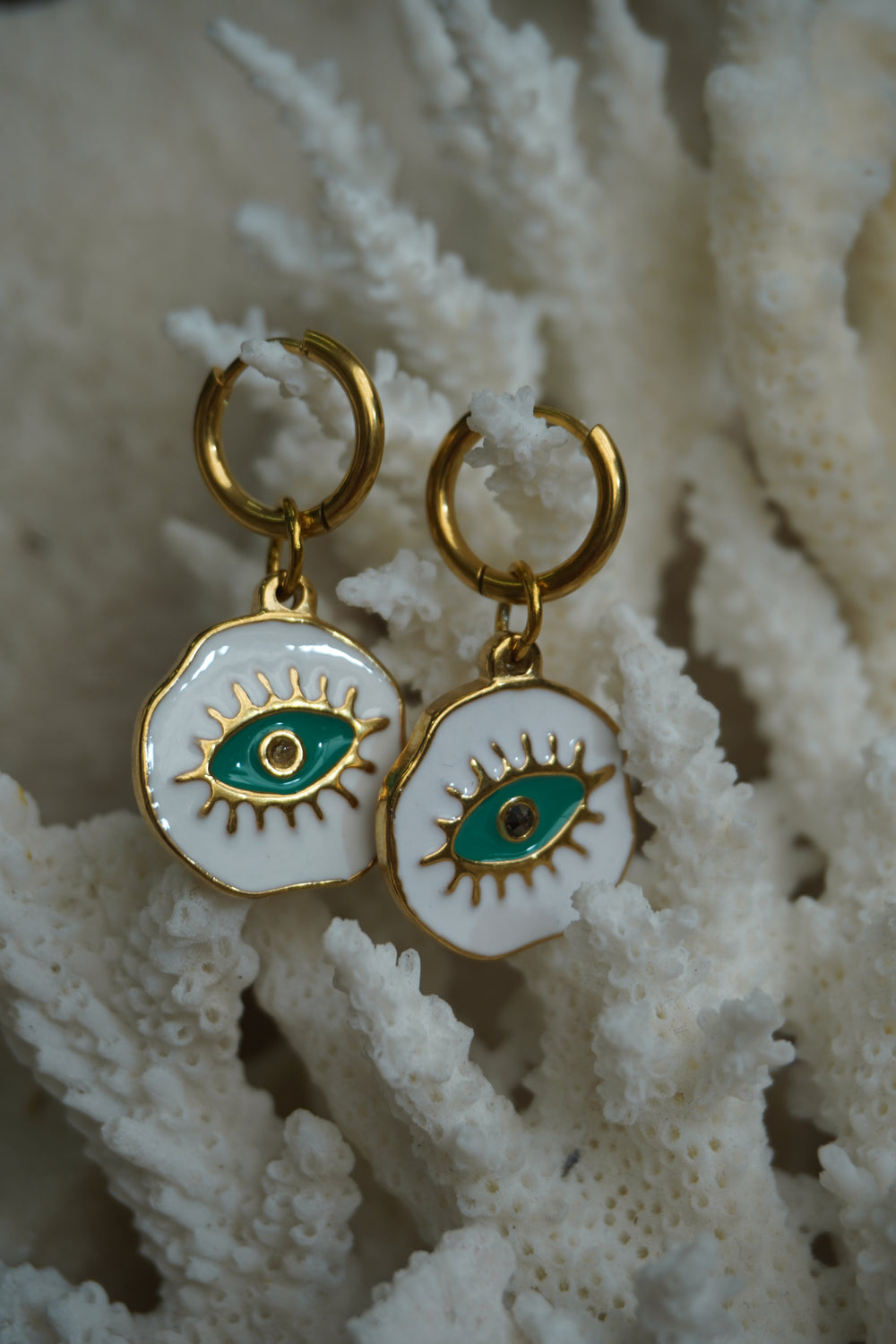 Gold-tone hoops with irregular white disc charms, green eye motifs and raised lashes.