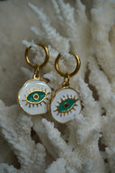 Gold-tone hoops with irregular white disc charms, green eye motifs and raised lashes.