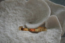 Gold-tone open cuff with a smooth flat band and reflective surface.