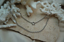 Silver-tone layered chain necklace arrangement with oval links and a circular clasp detail on the upper line.