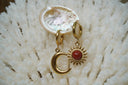 Gold-tone hoop earrings with a red-centred sun charm and a smooth crescent moon charm.