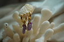 Gold-tone hoops with small round purple beads, larger irregular purple drops and reflective charms.