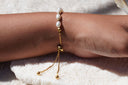 Back view of a white oval-bead bracelet on a wrist, showing a round connector and two gold-tone chain ends with ball tips.