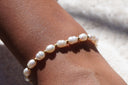 White oval-bead bracelet with small gold-tone spacers, shown on a wrist.