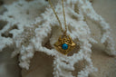 Alternate view: gold-tone chain necklace with an eye-shaped pendant, bright blue centre, ridged lower border and small skull motifs above.