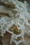 Gold-tone chain necklace with an eye-shaped pendant, bright blue centre, ridged lower border and small skull motifs above.