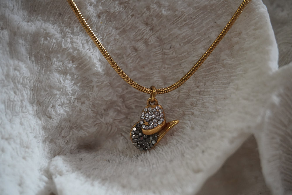 Gold-tone necklace with a miniature western hat pendant covered in dark and bright details.
