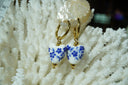 Alternate view: gold-tone hoop earrings with white heart-shaped drops patterned with blue flowers and stems.