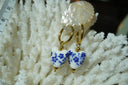 Gold-tone hoop earrings with white heart-shaped drops patterned with blue flowers and stems.