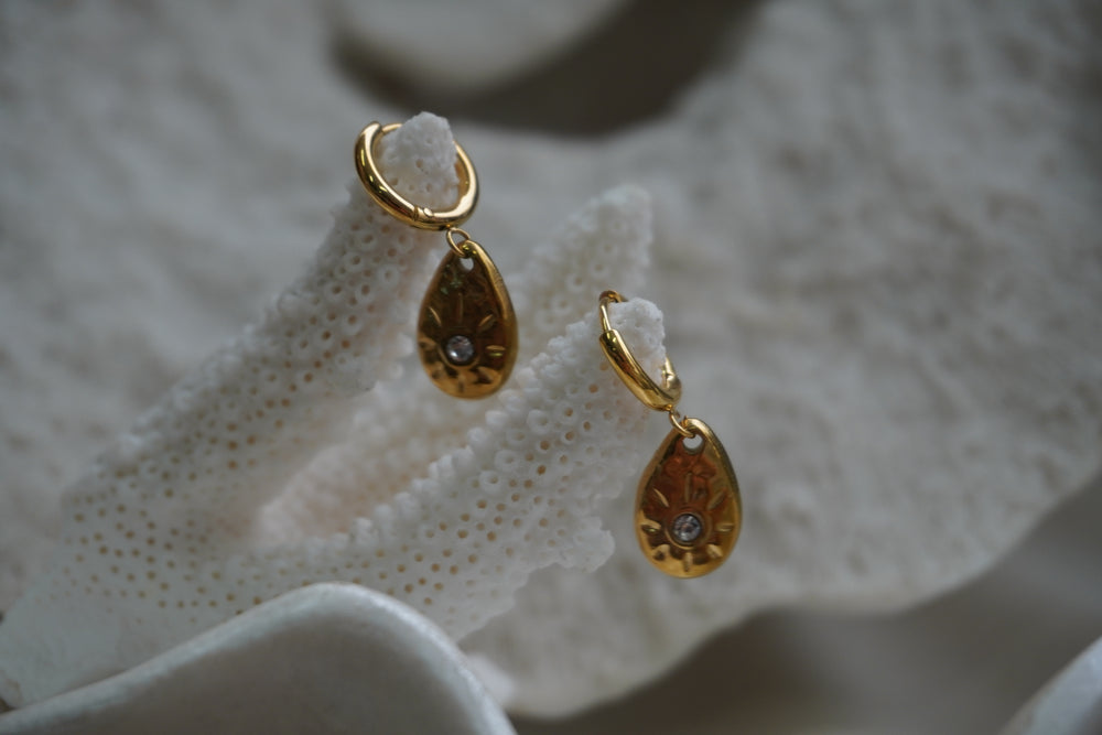 Gold-tone hoop earrings with teardrop charms, round clear accents and sunburst markings.
